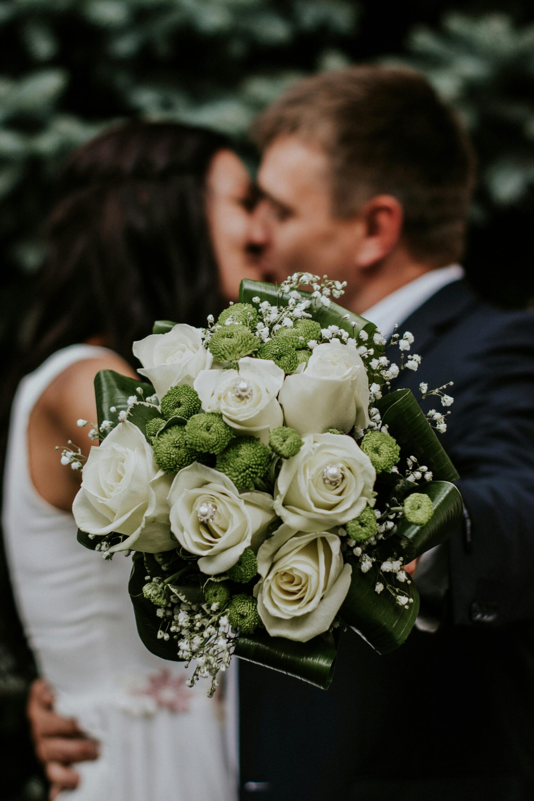 pexels-photo-948185-948185 A couple embracing with a focus on a white rose and green floral wedding bouquet.